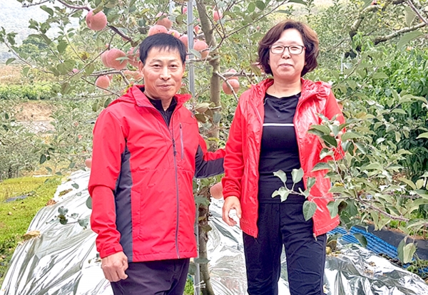 이달의 충북농협 새농민상을 수상한 김오달(왼쪽)·전재동씨 부부가 사과 과수원을 배경으로 기념촬영을 하고 있다.